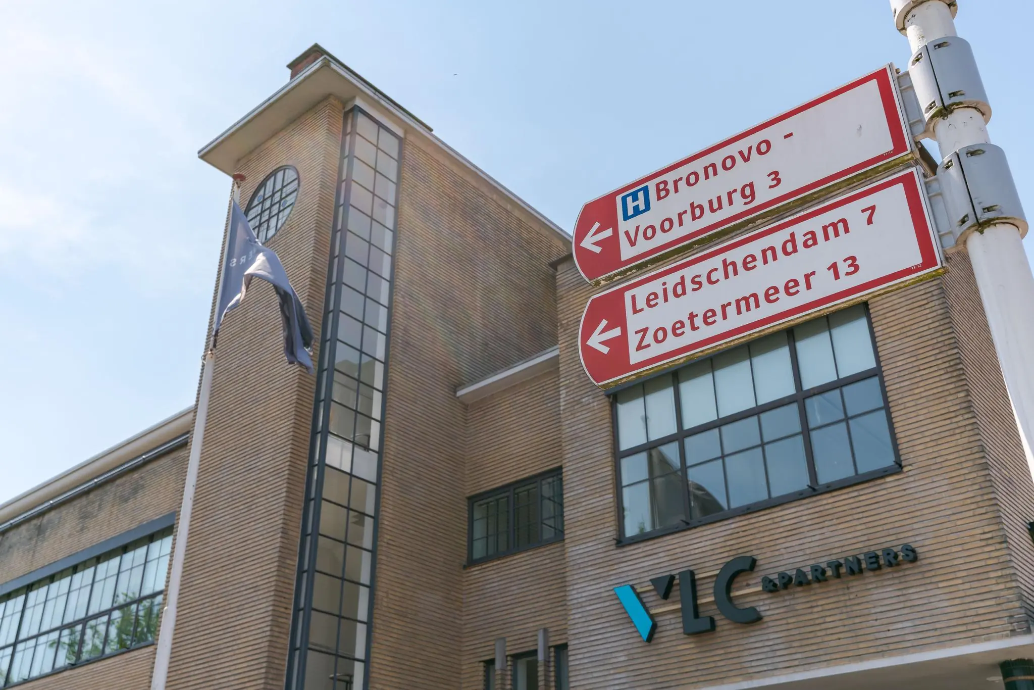 Wegwijzer met richtingen naar Bronovo, Voorburg, Leidschendam en Zoetermeer voor een modern kantoorgebouw aan de Van Alkemadelaan.